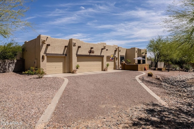 pueblo revival-style home with stucco siding, an attached garage, and driveway