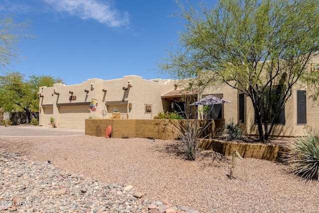 pueblo revival-style home featuring fence, an attached garage, driveway, and stucco siding