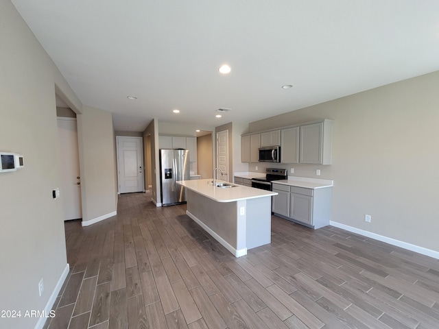 kitchen with sink, light hardwood / wood-style flooring, gray cabinets, a center island with sink, and appliances with stainless steel finishes