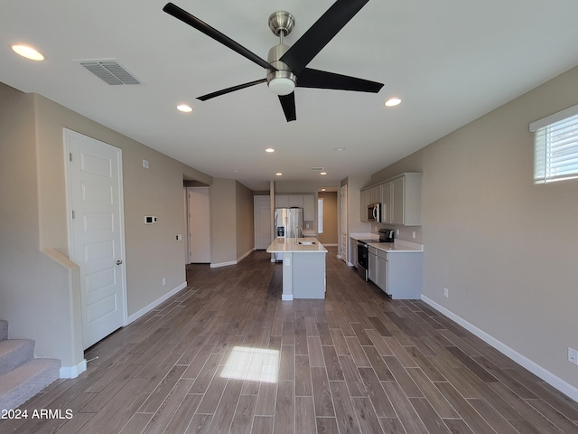 kitchen with a center island with sink, dark hardwood / wood-style floors, ceiling fan, white cabinetry, and stainless steel appliances