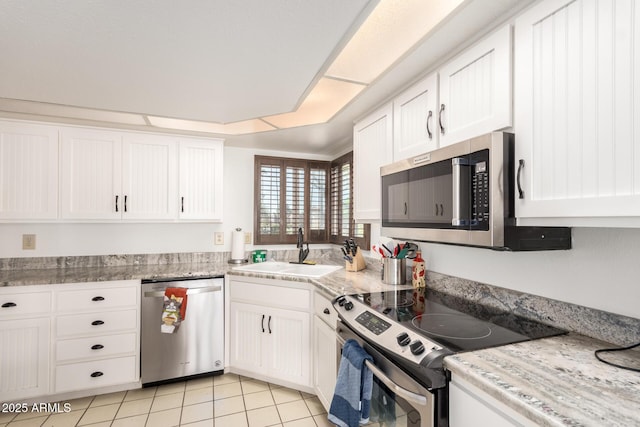 kitchen with appliances with stainless steel finishes, sink, white cabinets, light tile patterned floors, and light stone countertops