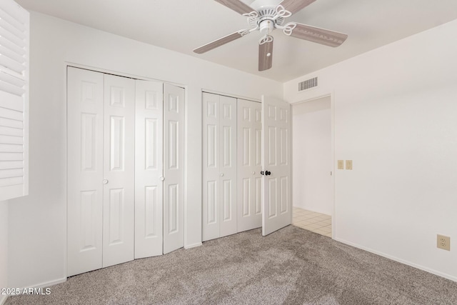 unfurnished bedroom with multiple closets, light colored carpet, and ceiling fan