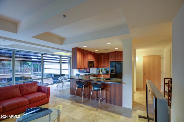 kitchen featuring floor to ceiling windows, black appliances, a kitchen breakfast bar, a raised ceiling, and sink