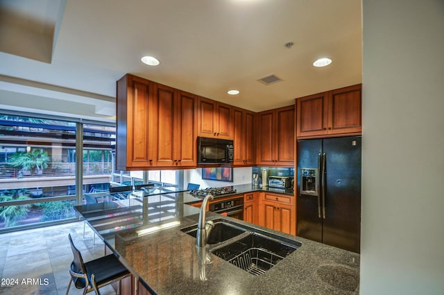 kitchen featuring dark stone counters, black appliances, a kitchen breakfast bar, sink, and kitchen peninsula