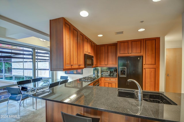 kitchen featuring black appliances, dark stone countertops, kitchen peninsula, and sink