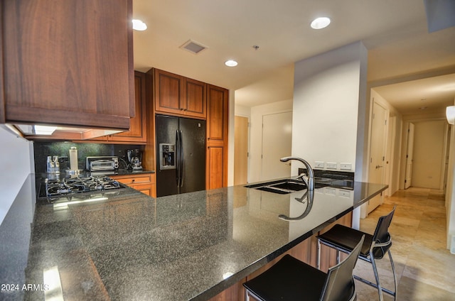 kitchen with a kitchen bar, black fridge with ice dispenser, kitchen peninsula, and stainless steel gas stovetop