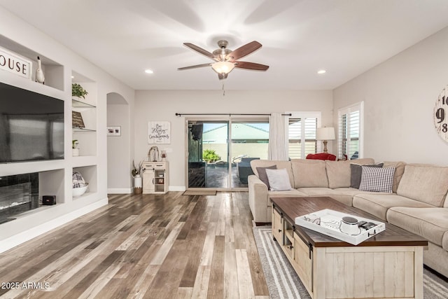 living room featuring hardwood / wood-style flooring, built in shelves, and ceiling fan