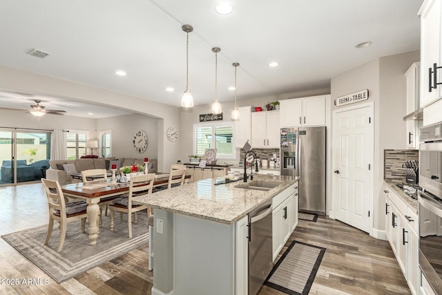 kitchen with decorative backsplash, stainless steel appliances, a center island with sink, white cabinetry, and hanging light fixtures