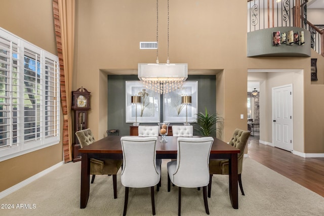 dining room with hardwood / wood-style floors, ceiling fan with notable chandelier, and a high ceiling