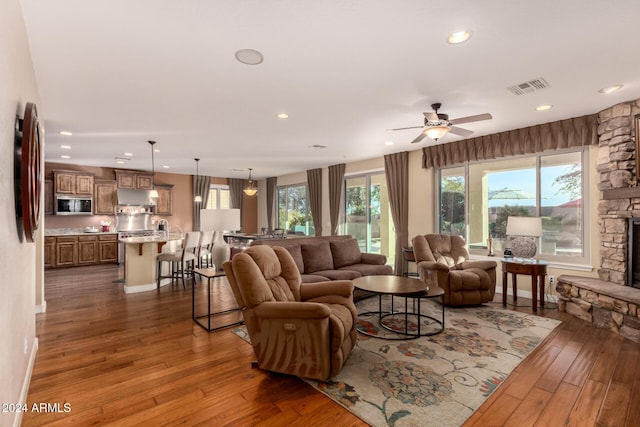 living room with ceiling fan, a stone fireplace, dark hardwood / wood-style flooring, and a wealth of natural light