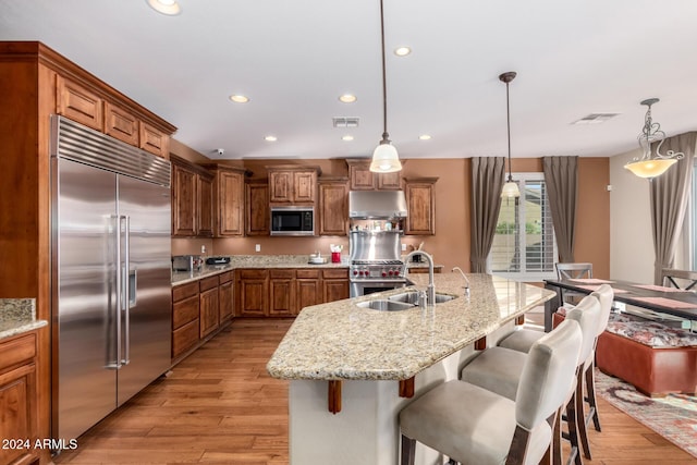 kitchen featuring a center island with sink, decorative light fixtures, light hardwood / wood-style floors, and stainless steel built in refrigerator