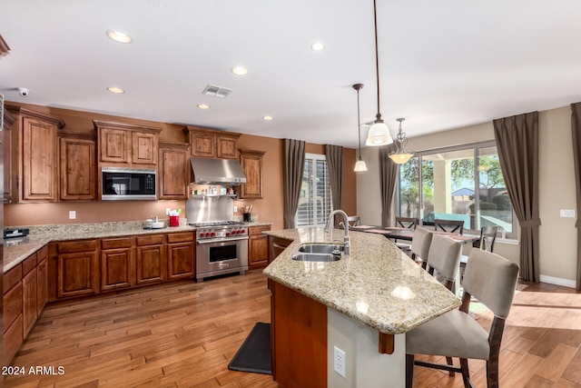 kitchen featuring exhaust hood, sink, light wood-type flooring, an island with sink, and premium stove