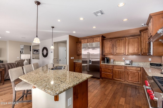 kitchen with high end appliances, dark wood-type flooring, sink, and an island with sink