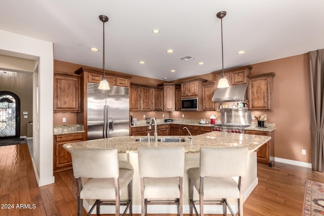 kitchen featuring sink, hanging light fixtures, a center island with sink, exhaust hood, and appliances with stainless steel finishes