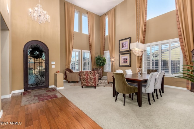 dining area with a notable chandelier, a healthy amount of sunlight, wood-type flooring, and a high ceiling