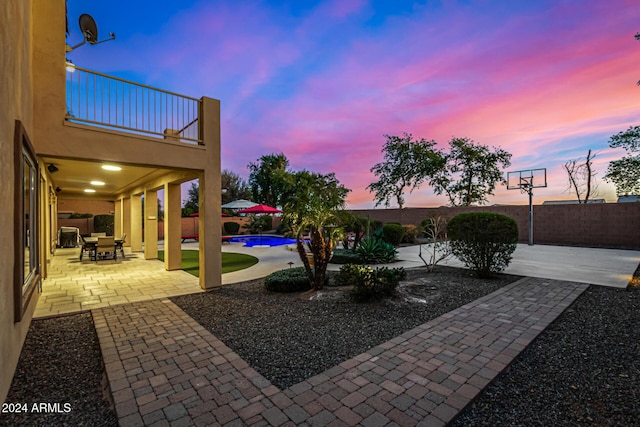 patio terrace at dusk with a balcony and a fenced in pool