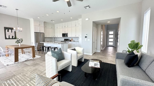 living area with visible vents, a wealth of natural light, and ceiling fan with notable chandelier