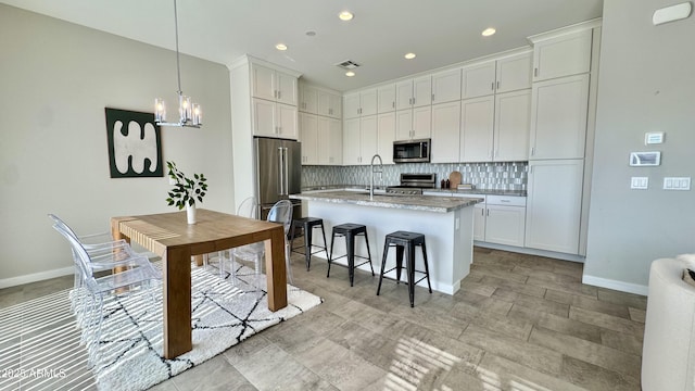 kitchen featuring a breakfast bar area, white cabinets, appliances with stainless steel finishes, tasteful backsplash, and a center island with sink