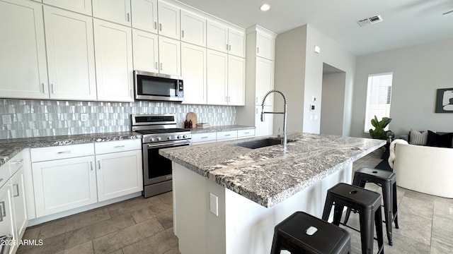 kitchen featuring light stone counters, a sink, white cabinets, appliances with stainless steel finishes, and decorative backsplash