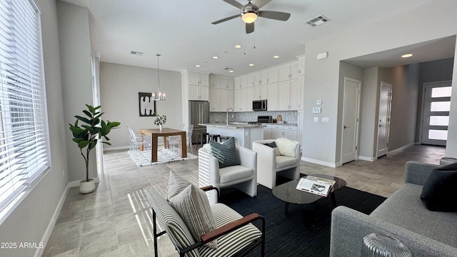 living area with ceiling fan with notable chandelier, recessed lighting, visible vents, and baseboards