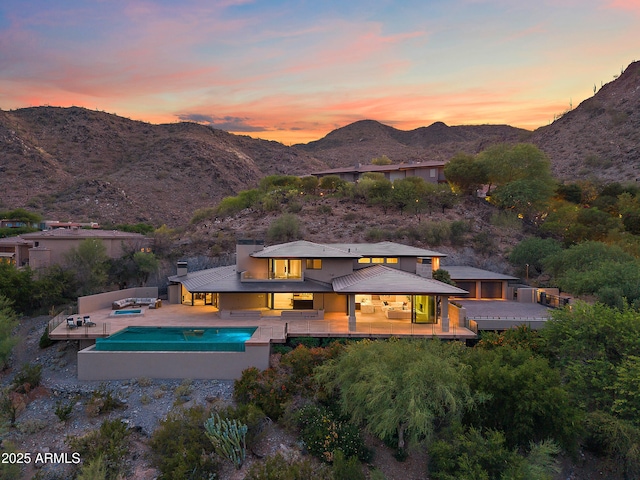 rear view of house with outdoor lounge area, a mountain view, an outdoor pool, metal roof, and a patio