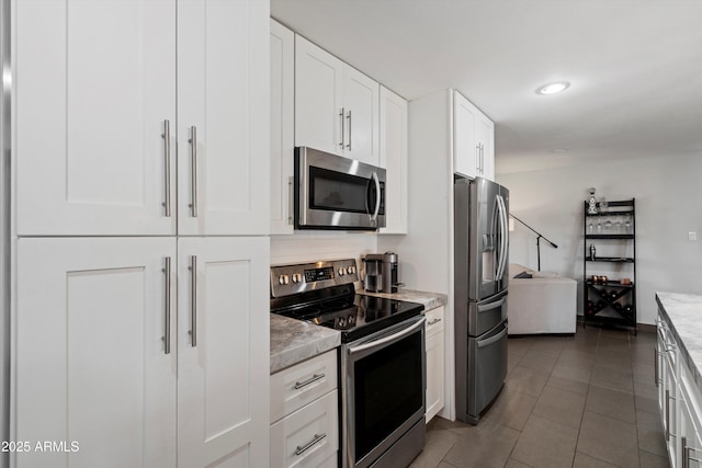 kitchen with white cabinets, light stone counters, appliances with stainless steel finishes, and dark tile patterned flooring