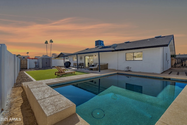 pool at dusk with a yard, a patio, an outdoor hangout area, and a storage shed