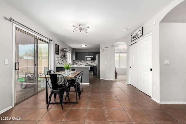 dining room with a wealth of natural light, arched walkways, dark tile patterned flooring, and baseboards