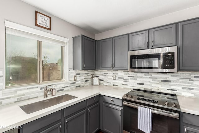 kitchen with a sink, light countertops, appliances with stainless steel finishes, gray cabinets, and tasteful backsplash