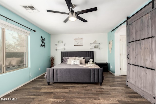 bedroom featuring ceiling fan, a barn door, wood finished floors, visible vents, and baseboards