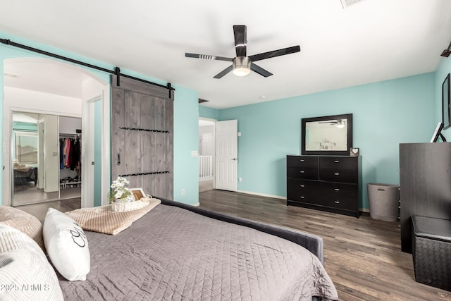 bedroom featuring a walk in closet, wood finished floors, baseboards, and a barn door