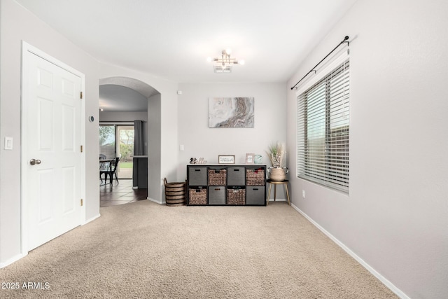 empty room featuring carpet floors, arched walkways, and baseboards