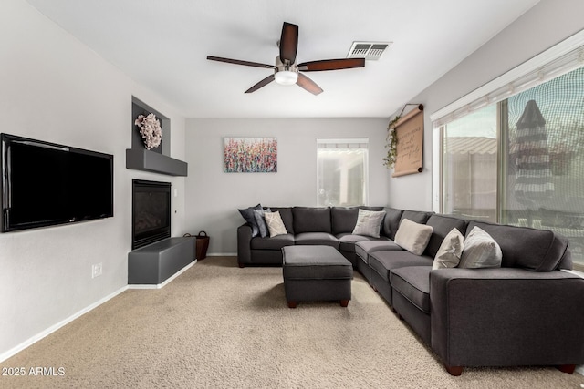 living area with baseboards, visible vents, ceiling fan, and a glass covered fireplace