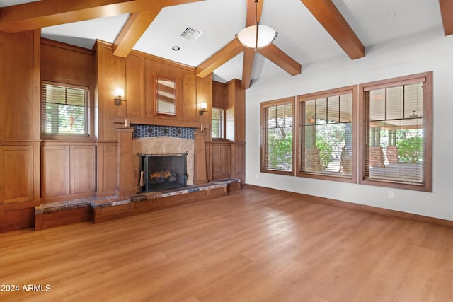 unfurnished living room featuring a tile fireplace, beam ceiling, light hardwood / wood-style flooring, and wood walls