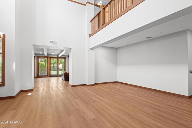 unfurnished living room with french doors, light hardwood / wood-style floors, and a high ceiling