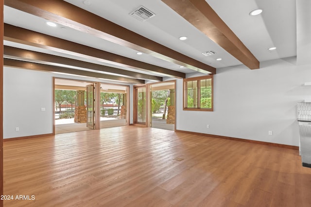 unfurnished living room featuring beamed ceiling and light wood-type flooring