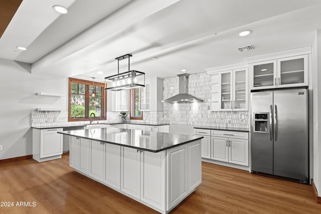 kitchen with stainless steel refrigerator with ice dispenser, a kitchen island, white cabinetry, and wall chimney exhaust hood