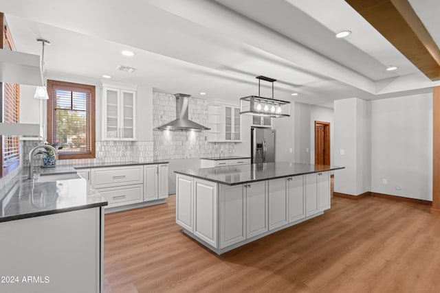 kitchen with sink, wall chimney range hood, a kitchen island, stainless steel refrigerator with ice dispenser, and white cabinets