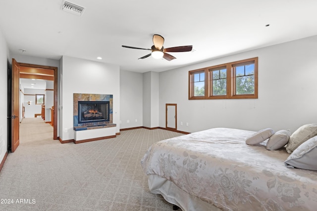 carpeted bedroom featuring a tiled fireplace and ceiling fan