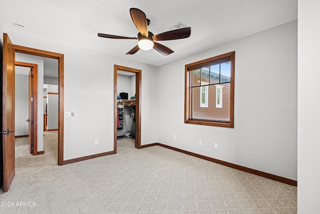 unfurnished bedroom featuring ceiling fan, light colored carpet, a walk in closet, and a closet