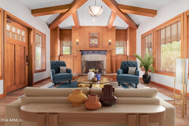 living room featuring a tile fireplace, light wood-type flooring, vaulted ceiling with beams, and a healthy amount of sunlight