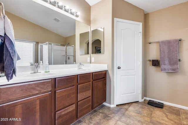 bathroom featuring double vanity, a stall shower, a sink, and baseboards