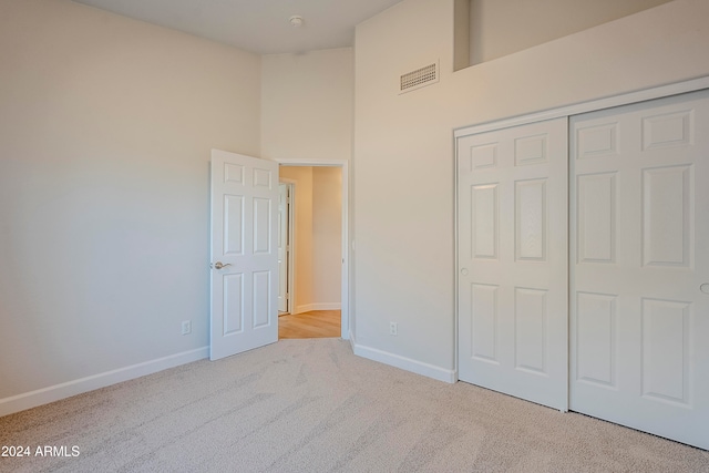 unfurnished bedroom with a towering ceiling, light carpet, and a closet