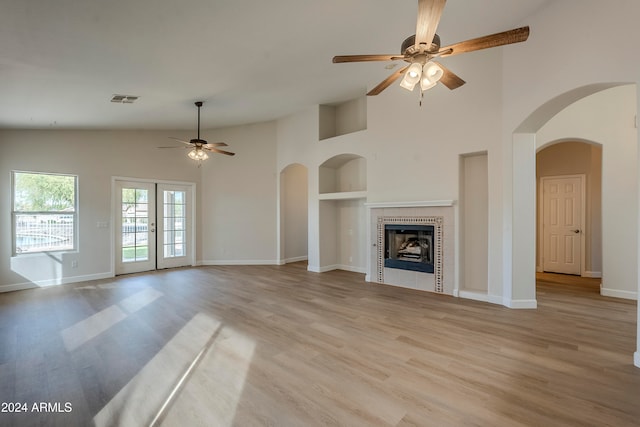 unfurnished living room featuring french doors, ceiling fan, built in shelves, a fireplace, and light hardwood / wood-style floors