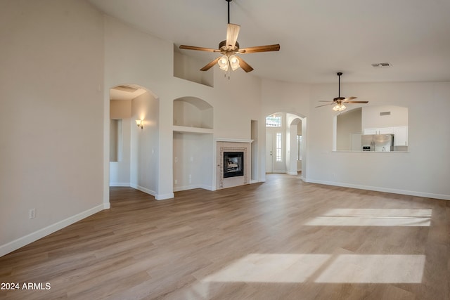 unfurnished living room featuring ceiling fan, light hardwood / wood-style floors, a towering ceiling, and built in features