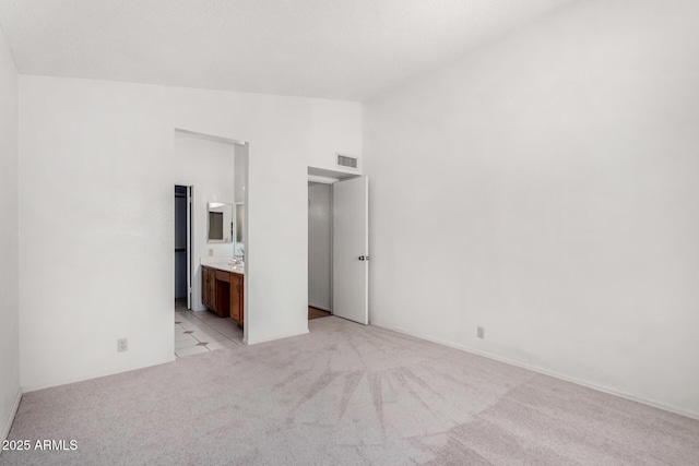 unfurnished bedroom featuring lofted ceiling, light carpet, visible vents, and ensuite bath