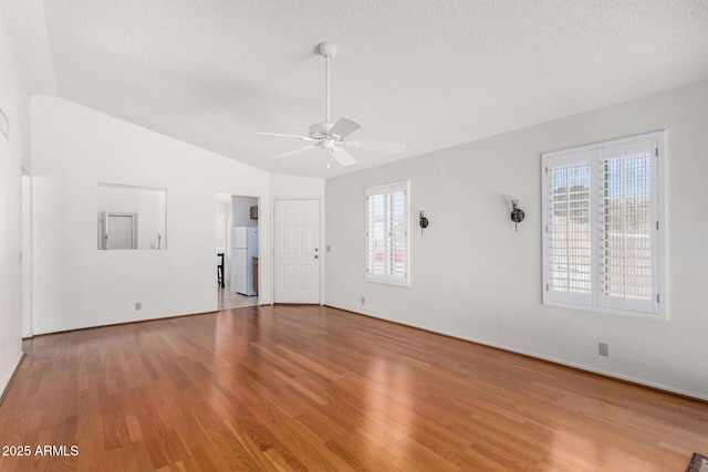 unfurnished room featuring light wood-style flooring, a textured ceiling, vaulted ceiling, and a wealth of natural light