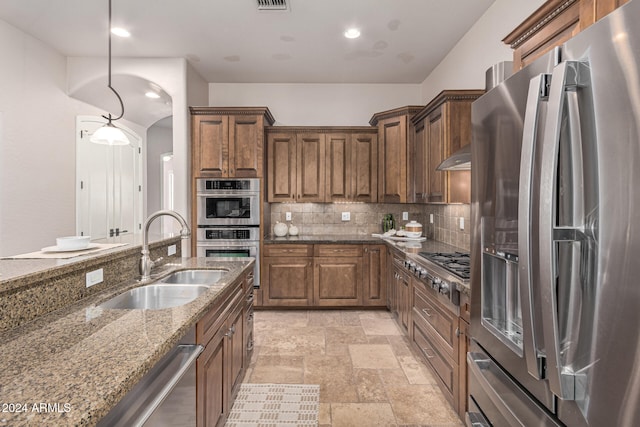 kitchen featuring sink, dark stone counters, decorative light fixtures, decorative backsplash, and appliances with stainless steel finishes