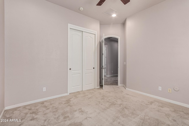 unfurnished bedroom with a closet, light colored carpet, and ceiling fan