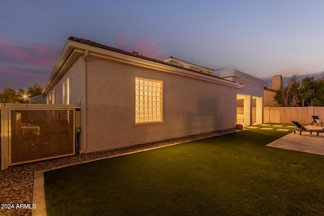 property exterior at dusk featuring a patio area and a yard